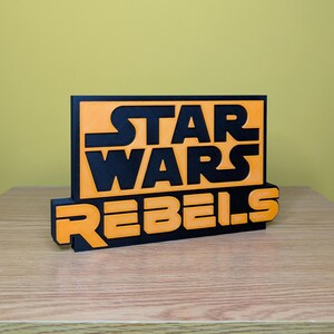 May include: A black and orange 3D printed sign with the text "Star Wars Rebels".