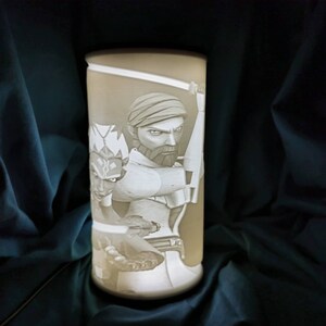 May include: A white ceramic lamp with a 3D image of two characters from the Star Wars: The Clone Wars animated series. The characters are a Jedi Master and his Padawan, both holding lightsabers.
