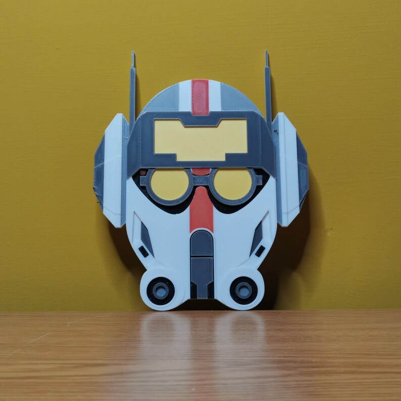 Pu&ograve; includere: Un casco stampato in 3D bianco, grigio e rosso con una visiera gialla. Il casco ha un design che ricorda un casco da pilota.