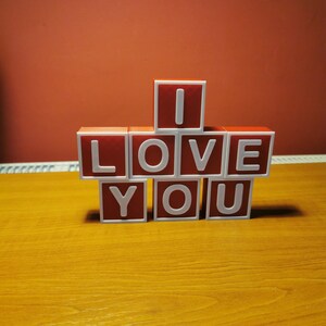 May include: Red letter blocks spelling out "I LOVE YOU" on a wooden surface.