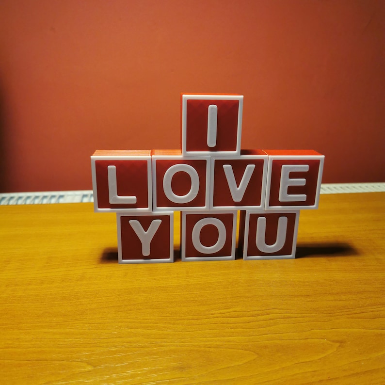 May include: Red letter blocks spelling out "I LOVE YOU" on a wooden surface.