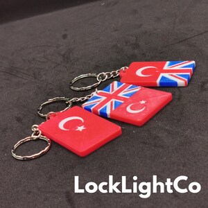 May include: Three keychains with red, white, and blue flags. The keychains feature the Turkish flag and the Union Jack flag. The text "LockLightCo" is visible at the bottom of the image.