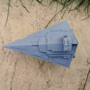 May include: A gray 3D printed model of a Star Wars spaceship. The model is detailed and has a sharp, angular design.