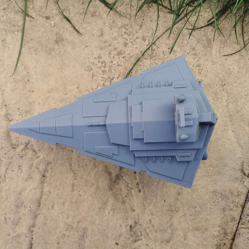 May include: A gray 3D printed model of a Star Wars spaceship. The model is detailed and has a sharp, angular design.