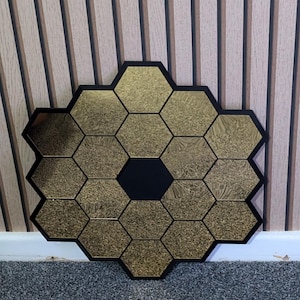 May include: A gold hexagonal mirror with a black center, made of multiple smaller hexagonal mirrors. The mirror is hanging on a striped wall.