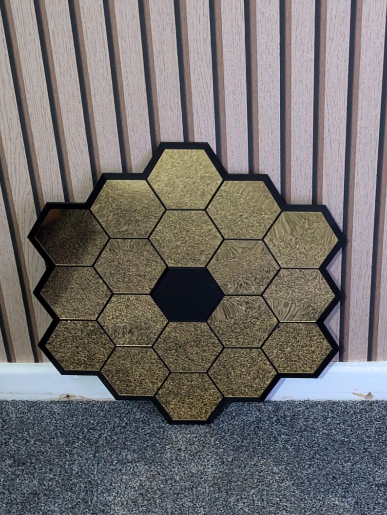 May include: A gold hexagonal mirror with a black center, made of multiple smaller hexagonal mirrors. The mirror is hanging on a striped wall.