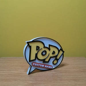 May include: A white, yellow, and black 3D printed Pop! figure with a speech bubble that says "CUSTOM NAME".