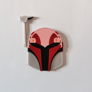May include: A 3D printed Mandalorian helmet with a red and black design. The helmet has a gray base and a pink top with orange accents.