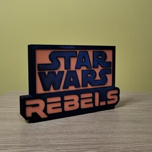 May include: A black and orange 3D printed sign with the text "Star Wars Rebels".