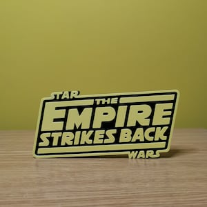 May include: A yellow and black sign with the text "STAR WARS THE EMPIRE STRIKES BACK" in a bold, black font.