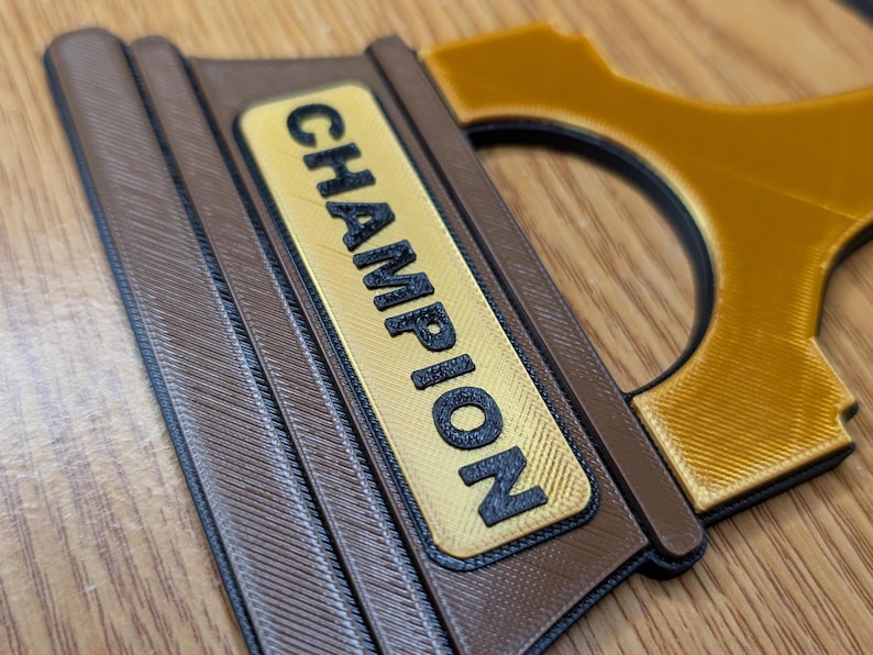 May include: Close-up of a brown and gold trophy with the word "CHAMPION" printed on the front.