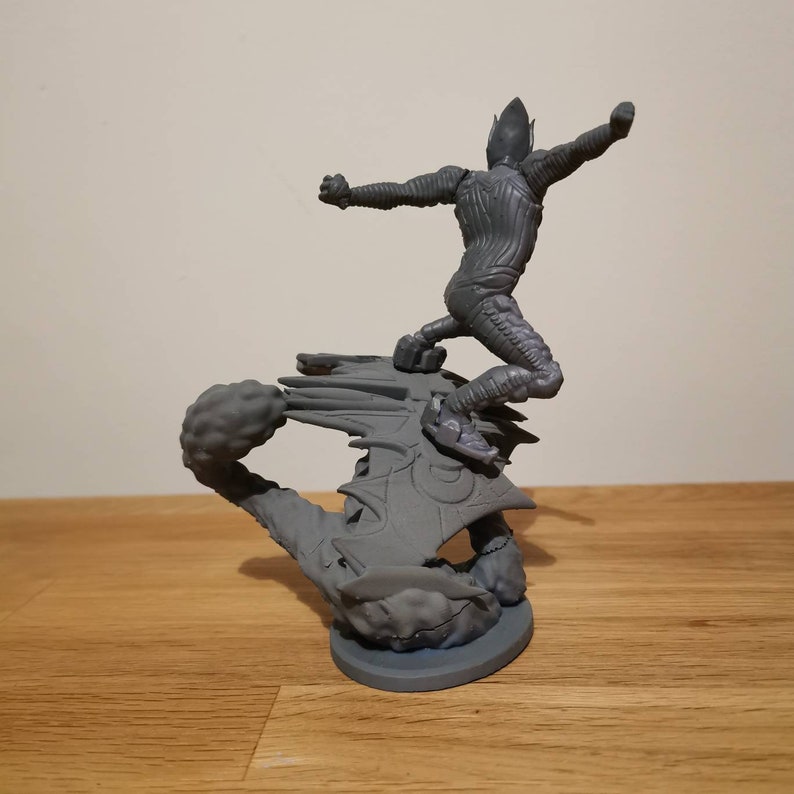 May include: A gray 3D printed figurine of a humanoid figure riding a winged creature. The figure is posed with one arm outstretched and the other bent at the elbow. The winged creature has a long tail and is in mid-flight.