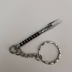 May include: A silver and black lightsaber keychain with a red gem. The keychain has a silver chain and a silver ring.