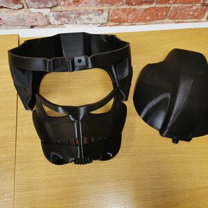 May include: Two black plastic pieces of a 3D printed helmet. The helmet has a face mask with a visor and a separate top piece.