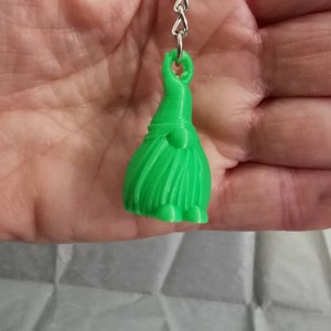 May include: A green gnome keyring with a long beard and a small hat. The gnome is made of plastic and has a silver chain attached to it.