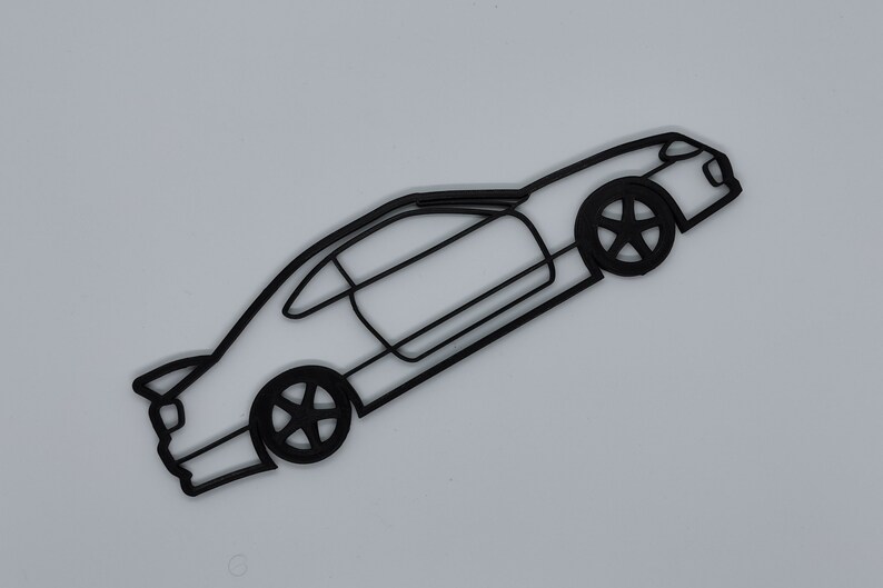 May include: Black line art silhouette of a sports car with a spoiler, side windows, and wheels. The car is facing the right side of the image and is angled slightly upward.