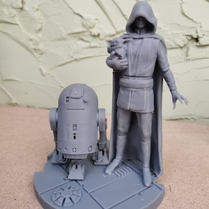 May include: A gray 3D printed figurine set featuring a hooded figure holding a small creature, a droid, and a circular base with a textured surface.