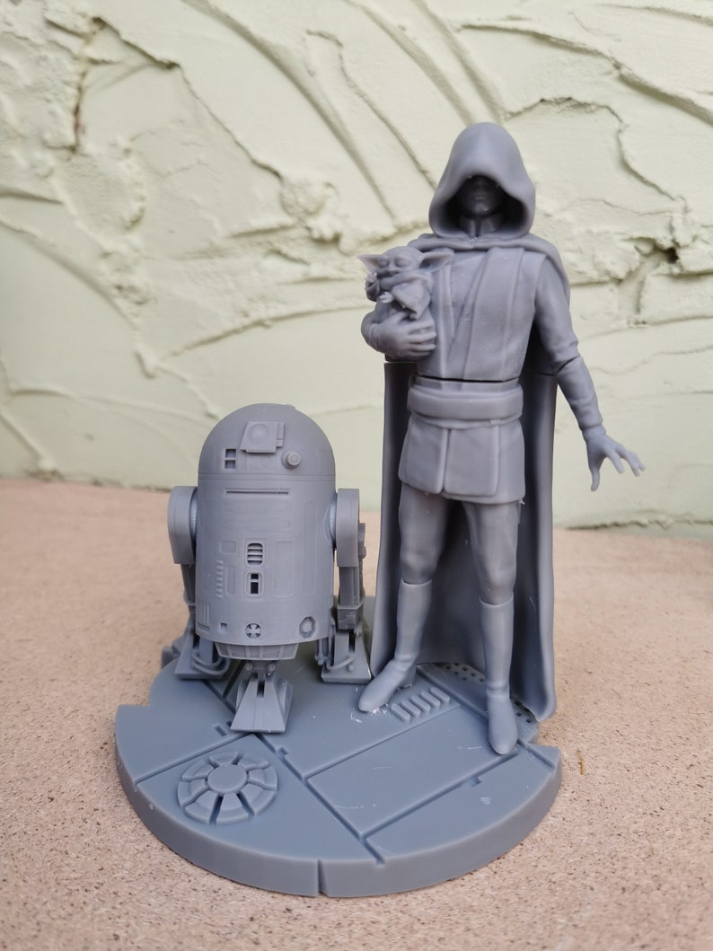 May include: A gray 3D printed figurine set featuring a hooded figure holding a small creature, a droid, and a circular base with a textured surface.