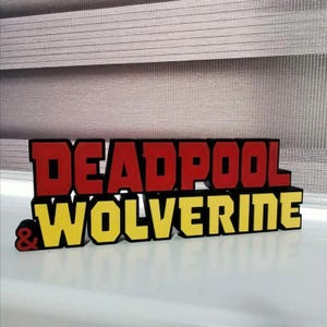 Może przedstawiać: Tabliczka 3D wydrukowana z napisem "DEADPOOL & WOLVERINE" w czerwonych i ż&oacute;łtych literach. Litery są wypukłe i mają czarny kontur.