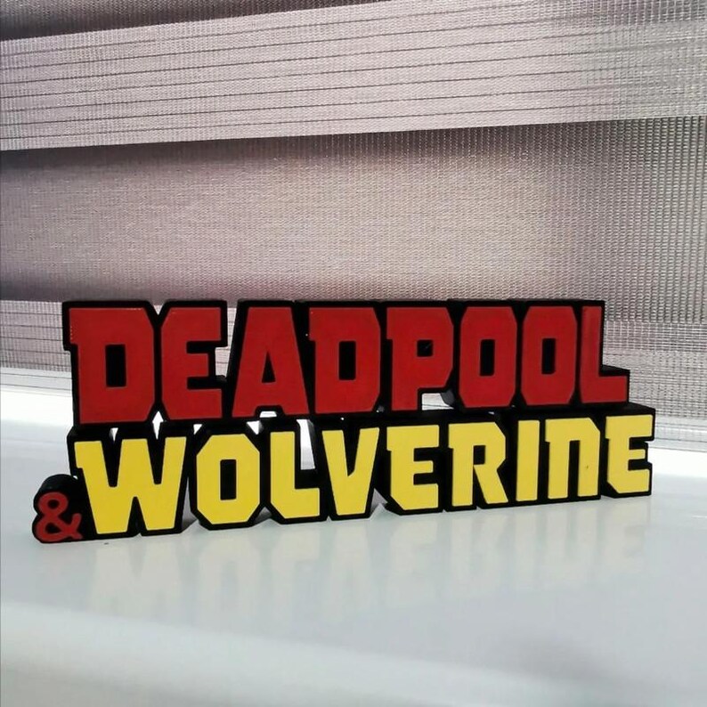Może przedstawiać: Tabliczka 3D wydrukowana z napisem "DEADPOOL & WOLVERINE" w czerwonych i ż&oacute;łtych literach. Litery są wypukłe i mają czarny kontur.
