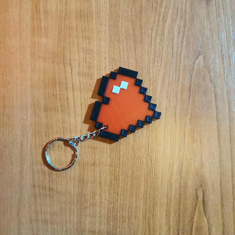 May include: A red pixelated heart keychain with a black border and a silver ring.