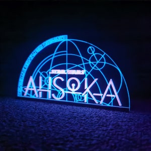 May include: A blue and white light-up sign with the text "STAR WARS" and "AHsoka" in a stylized font. The sign features a geometric design with circles and lines.