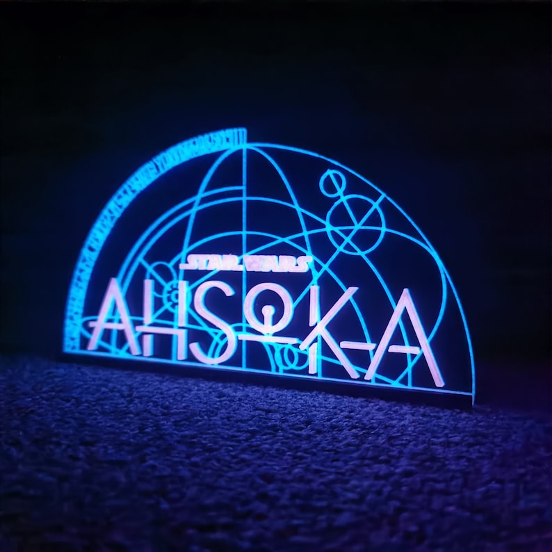 May include: A blue and white light-up sign with the text "STAR WARS" and "AHsoka" in a stylized font. The sign features a geometric design with circles and lines.