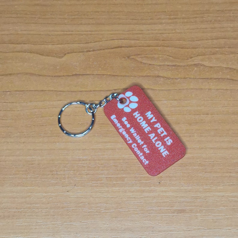 May include: Red rectangular keychain with white text that reads "My Pet is Home Alone" and "See Wallet for Emergency Contact". A paw print symbol is above the text.