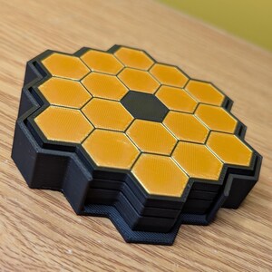 May include: A set of four black and gold honeycomb-shaped coasters. The coasters are stacked on top of each other.