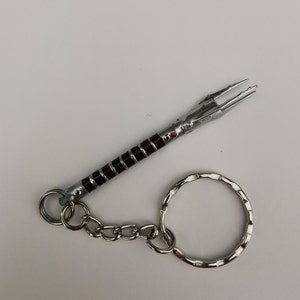Op de afbeelding: Een zilveren en zwarte lightsaber sleutelhanger met een rode edelsteen. De sleutelhanger heeft een zilveren ketting en een zilveren ring.