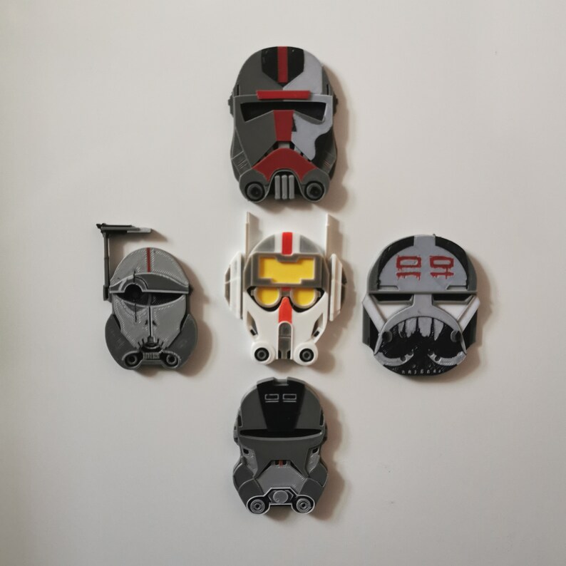 May include: Five Star Wars clone trooper helmet magnets in gray, white, and red. The helmets are all different designs and have different markings.