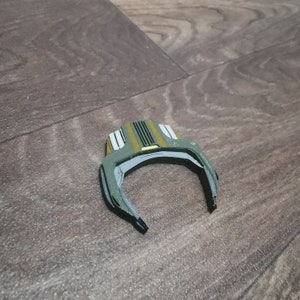 May include: A green and yellow plastic toy with a curved shape and a textured surface. The toy has a series of lines and a small yellow rectangle on the top.