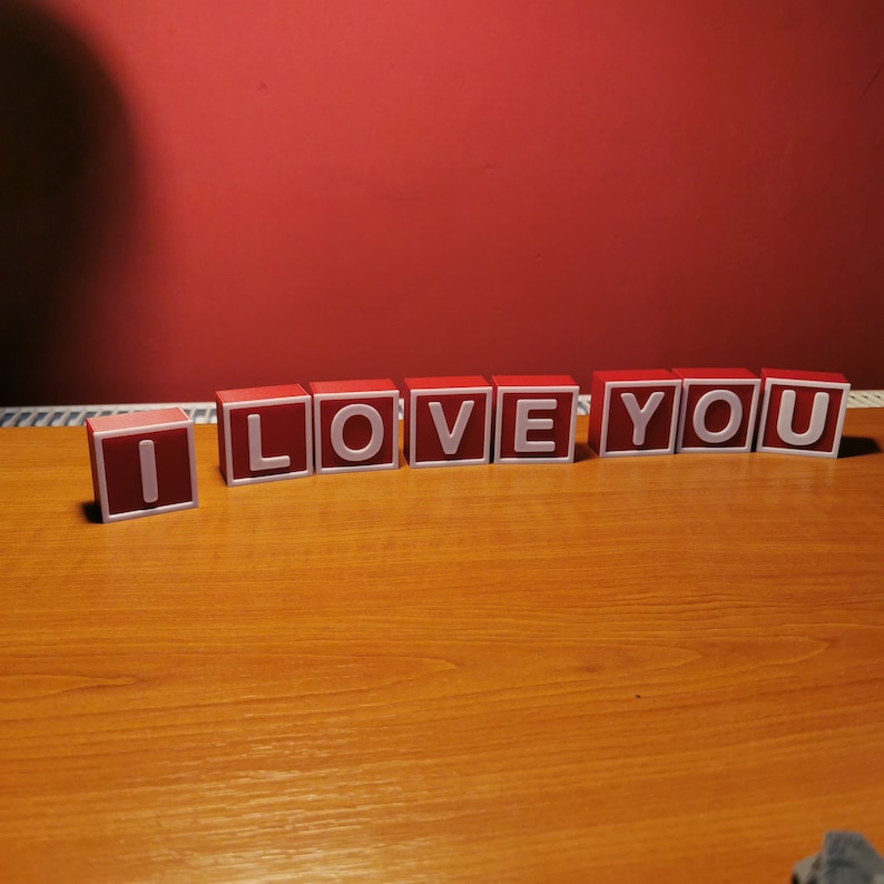 May include: Red wooden blocks spelling out the phrase "I LOVE YOU" on a wooden surface.