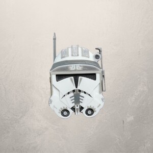 May include: A white and gray plastic clone trooper helmet with a black visor and a gray antenna. The helmet has a gray design on the front and a gray symbol on the top.