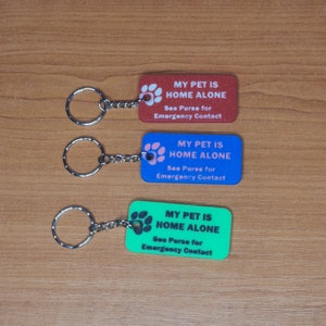 May include: Three keychains with rectangular tags that say "My Pet is Home Alone" in black text. The tags are red, blue, and green. Each tag has a paw print with a white outline.