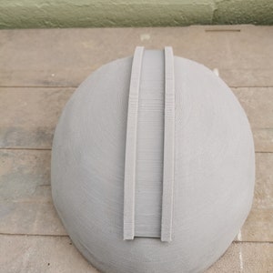 May include: A gray, 3D printed helmet with two raised ridges on the top.