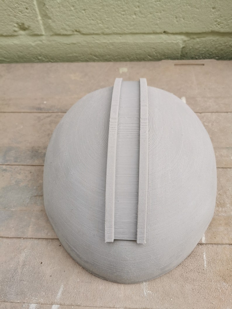 May include: A gray, 3D printed helmet with two raised ridges on the top.