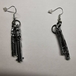 May include: A pair of silver earrings with a unique design. Each earring features a cluster of small, cylindrical shapes hanging from a silver hoop.