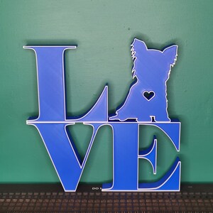 May include: Blue wooden cutout of the word "LOVE" with a white outline. A white silhouette of a dog is positioned on top of the "O" in the word.