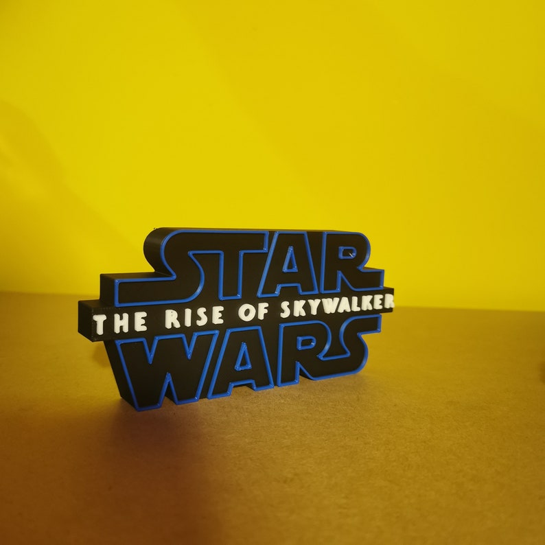 May include: A black and blue 3D printed logo for Star Wars: The Rise of Skywalker. The logo is on a brown surface.