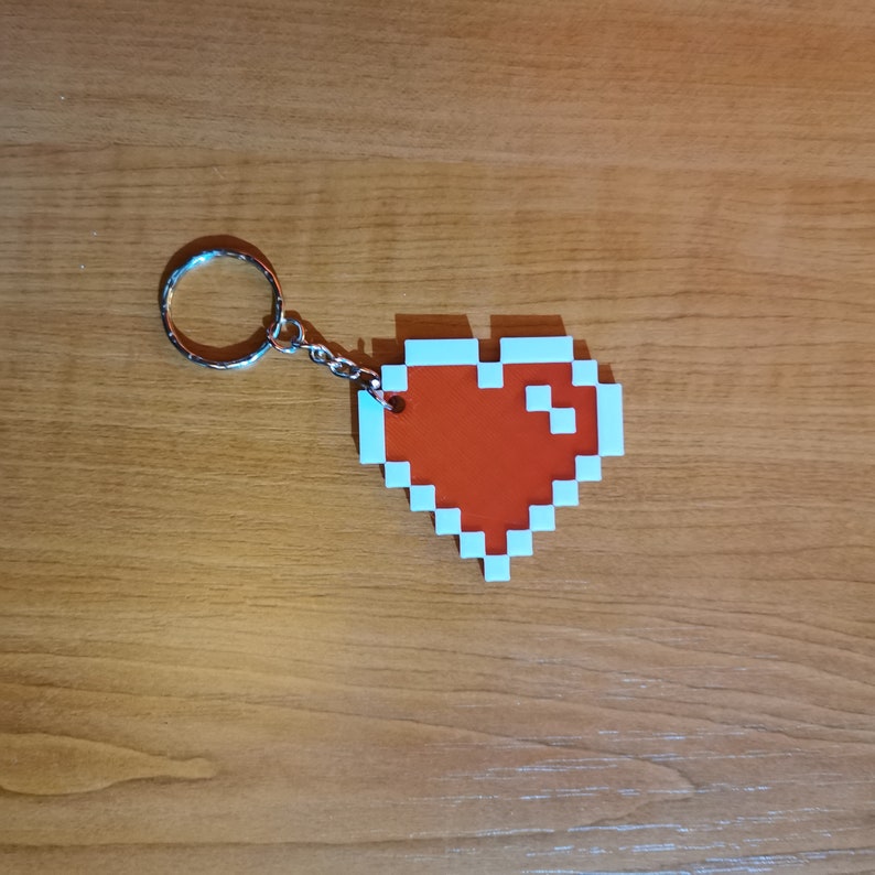 May include: A red pixel heart keychain with a silver metal ring. The heart is outlined in white.