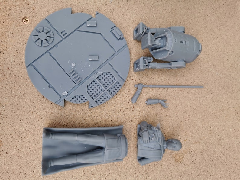May include: A set of gray 3D printed Star Wars figures, including a droid, a character, and a base. The figures are unpainted and ready to be assembled.