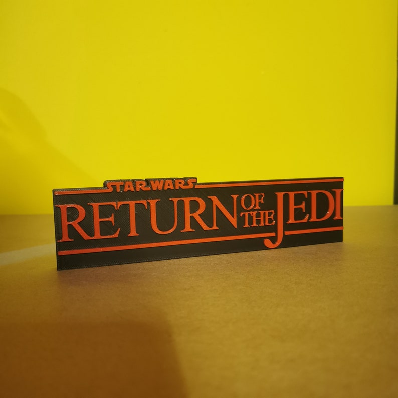 May include: A black and orange 3D printed sign that reads "STAR WARS RETURN OF THE JEDI".
