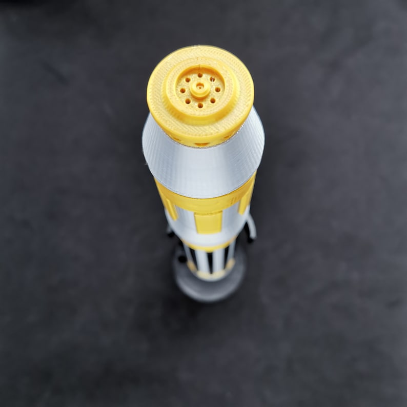 May include: A white and gold lightsaber with a yellow tip and a black handle. The lightsaber is a toy and is made of plastic.