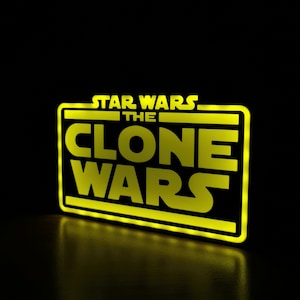 以下が含まれることがあります： 黒い長方形の枠の中に「STAR WARS THE CLONE WARS」という文字が書かれた黄色のネオンサインです。