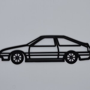 May include: Black outline of a classic sports car, featuring a two-door coupe design. The car's wheels and body lines are clearly defined against a white background. The image showcases a minimalist, graphic style.