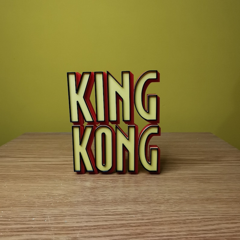 Pu&ograve; includere: Lettere 3D rosse e gialle che compongono la scritta "KING KONG" su una superficie di legno.