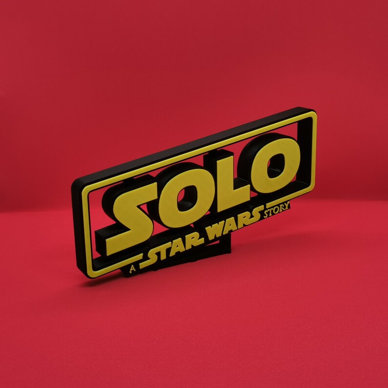 May include: A black and yellow 3D sign with the word "SOLO" in yellow letters and the text "A STAR WARS STORY" in black letters.