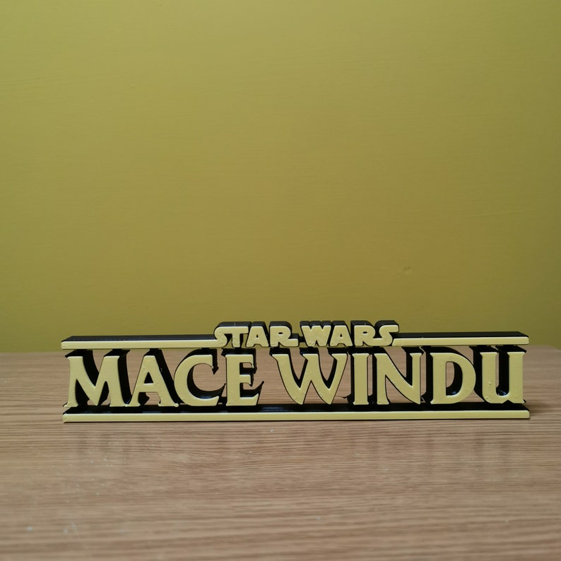 May include: A black and yellow 3D printed sign that reads "STAR WARS MACE WINDU".