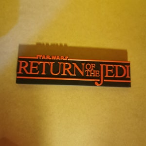 May include: A black and orange Star Wars Return of the Jedi logo on a black background.